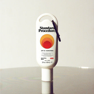 Standard Procedure SPF 50 Sunscreen 60ml travel tube with a carabiner clip on a reflective surface.