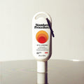 Standard Procedure SPF 50 Sunscreen 60ml travel-size tube with a carabiner clip on a reflective surface.