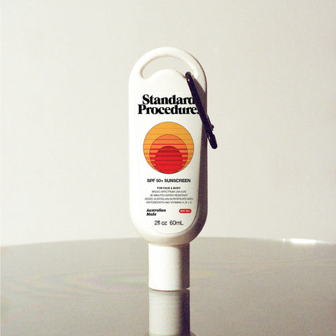 Standard Procedure SPF 50 Sunscreen 60ml travel-size tube with a carabiner clip on a reflective surface.