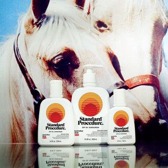 Standard Procedure SPF 50 Sunscreen collection in three sizes displayed in front of a white horse under a blue sky.