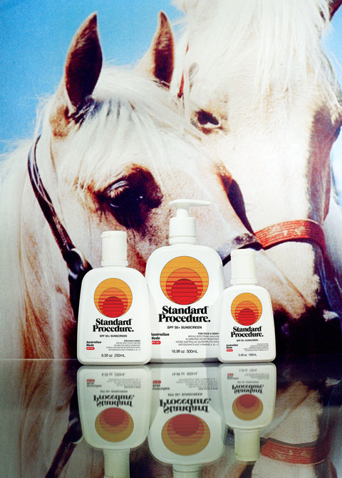 Standard Procedure SPF 50 Sunscreen collection in three sizes displayed in front of a white horse under a blue sky.