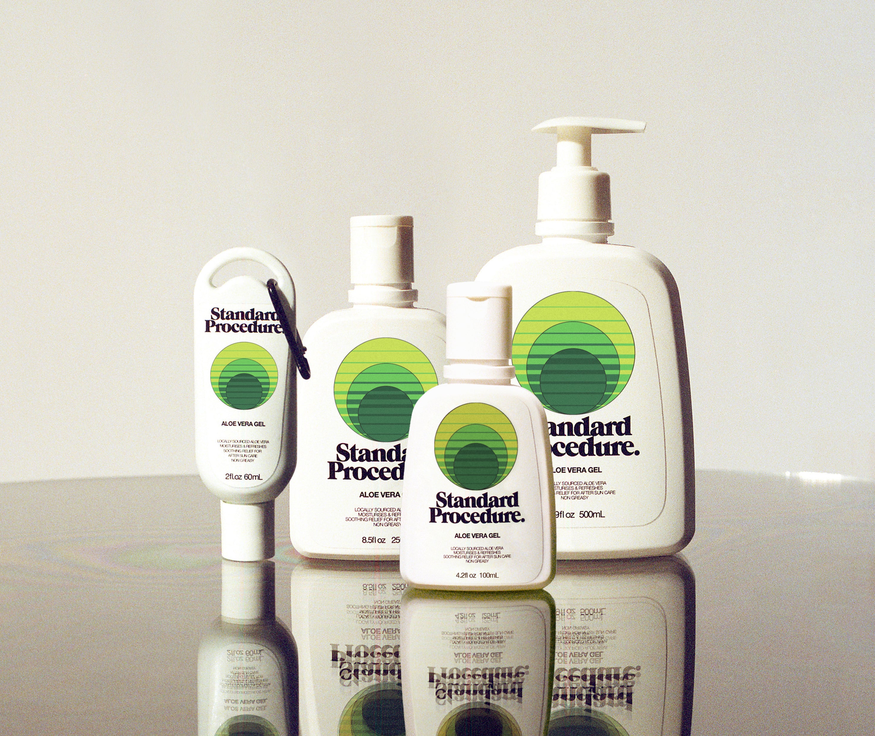 Aloe vera for sunburn bottles from Standard Procedure displayed on a reflective surface in various sizes, highlighting cooling, soothing, and moisturizing after-sun care made with locally sourced aloe