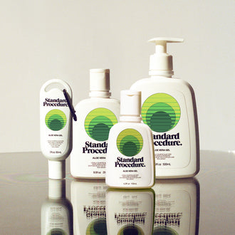 Aloe vera for sunburn bottles from Standard Procedure displayed on a reflective surface in various sizes, highlighting cooling, soothing, and moisturizing after-sun care made with locally sourced aloe