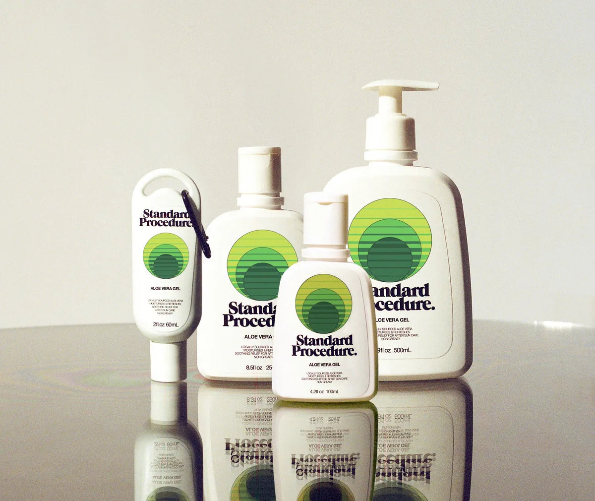 Aloe vera for sunburn bottles from Standard Procedure displayed on a reflective surface in various sizes, highlighting cooling, soothing, and moisturizing after-sun care made with locally sourced aloe