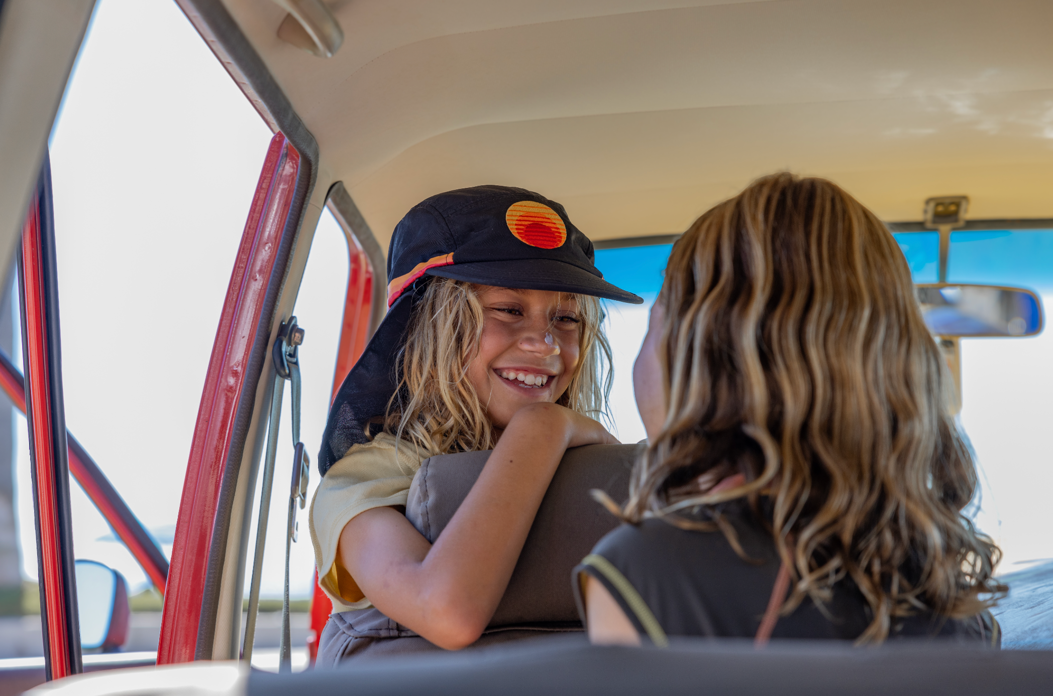 Women’s surf hat worn by a smiling girl inside a car, featuring a black brim and neck flap with the Standard Procedure logo, designed for stylish sun protection