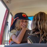 Women’s surf hat worn by a smiling girl inside a car, featuring a black brim and neck flap with the Standard Procedure logo, designed for stylish sun protection
