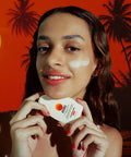 Woman holding a skincare product with a tropical background. Australian Sunscreen with skin benefits