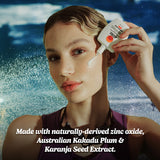 Australian mineral sunscreen applied to a woman’s cheek as she holds the bottle near her face, featuring ocean background and highlighting natural zinc oxide and Kakadu plum ingredients