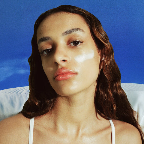 Woman with sheer sunscreen smudge on her face against a blue background