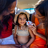 Mineral SPF 50 sunscreen being gently applied to a smiling child’s cheek by an adult, showing sun protection care during a family beach outing