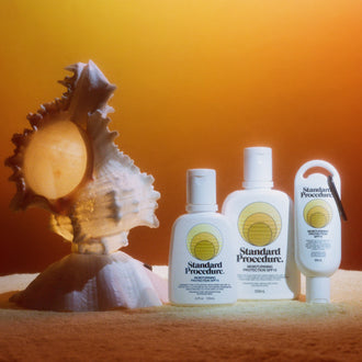 Three Standard Procedure SPF 15 moisturiser bottles beside a seashell on towel in sunset glow.