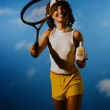 Tennis player in yellow shorts holds Standard Procedure SPF 15 moisturising sunscreen against a blue sky.