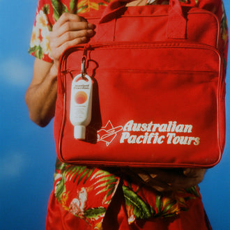 Best sunscreen lotion SPF 50 clipped to a red Australian Pacific Tours bag held by a person in tropical attire.