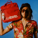 Best sunscreen from Australia clipped to a red Australian Pacific Tours bag held by a person in a floral shirt and sunglasses.