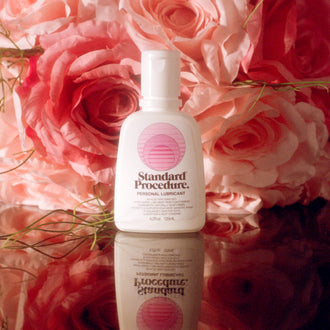 Pleasure Jelly aloe vera lubricant bottle styled against pink roses on a reflective surface.