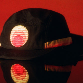 Black kids surf hat with embroidered sunset logo, reflected on a glossy red surface.