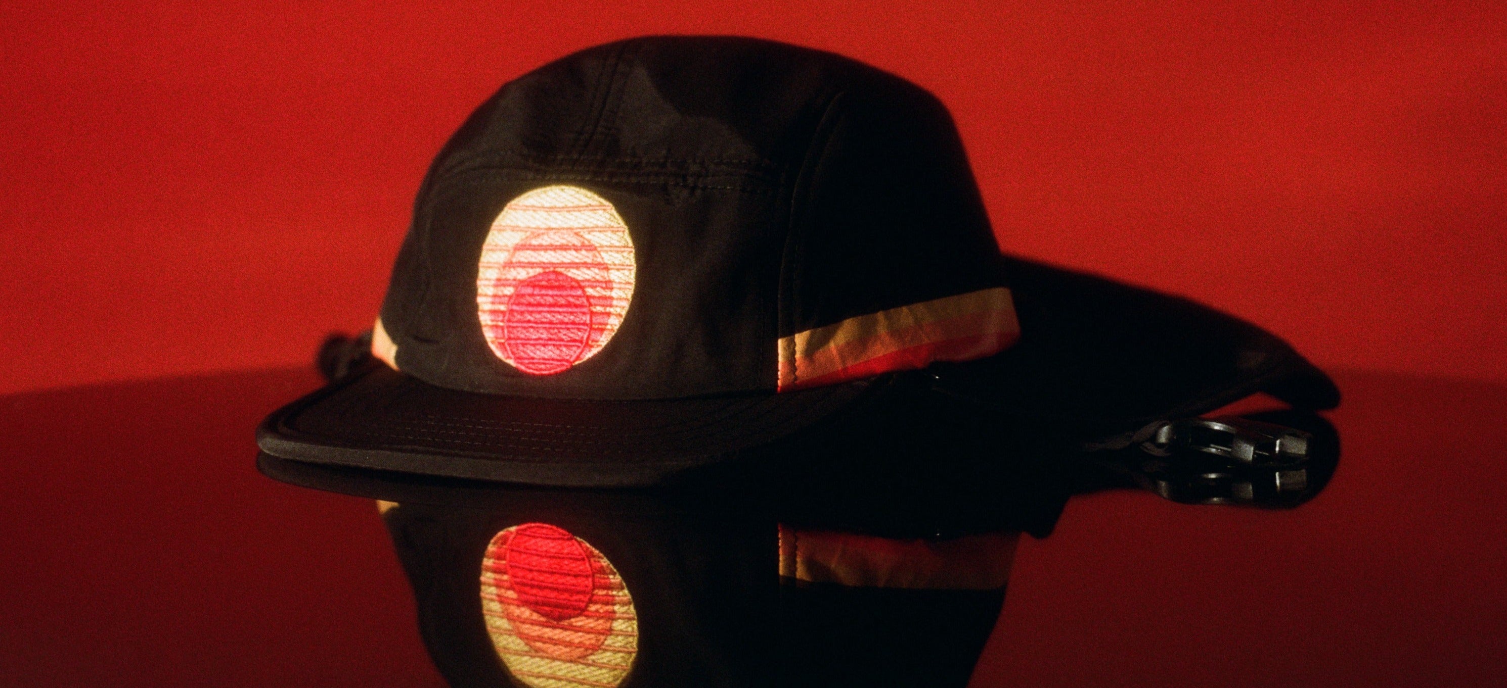 Black UPF 50+ five-panel sports hat with sunset patch and neck flap on red.