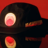 Black UPF 50+ five-panel sports hat with sunset patch and neck flap on red.