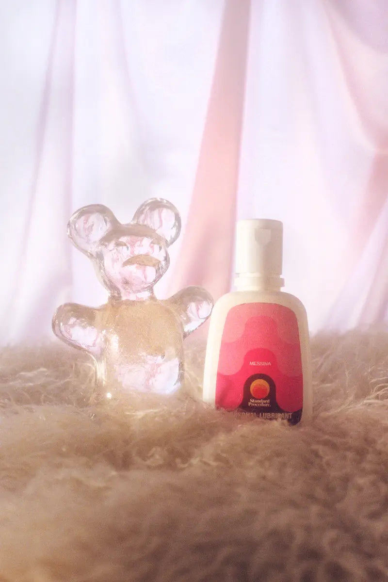 Standard Procedure x Messina personal lubricant bottle beside a clear gel bear on faux fur.