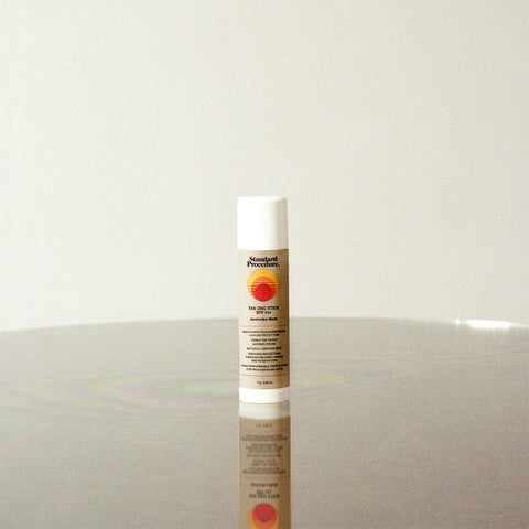 Zinc sunscreen stick standing upright on a reflective surface with minimalist beige background, featuring Standard Procedure label and sun logo design.