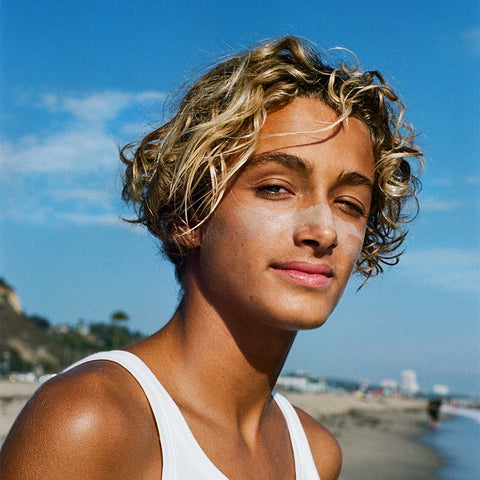Zinc oxide stick sunscreen on a beachgoer’s nose & cheeks in a close-up portrait by the ocean under a clear blue sky