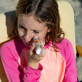 Zinc sunscreen stick applied by a young girl wearing a pink rash guard while sitting outdoors, protecting her face from sun exposure
