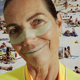 Zinc sunblock stick applied across a smiling woman’s nose & lips at a busy beach, wearing a yellow rash guard