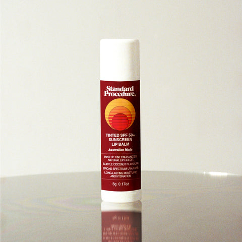 Standard Procedure Tinted SPF 50 Sunscreen Lip Balm with natural tint and coconut flavour on a reflective surface.