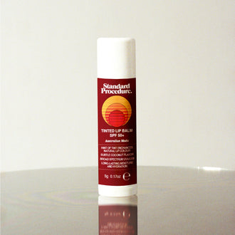 Standard Procedure Tinted Lip Balm SPF 50 with a hint of tint and coconut flavour on a reflective surface.