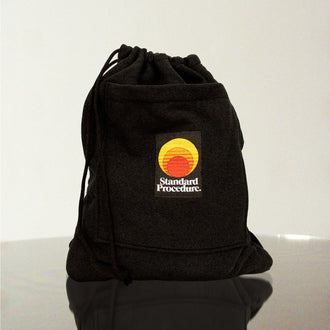 Standard Procedure black drawstring towel bag with an embroidered sunset logo patch on a reflective surface.