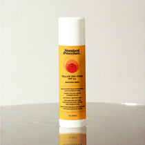 Yellow zinc SPF 50+ sunscreen stick by Standard Procedure on a reflective surface.
