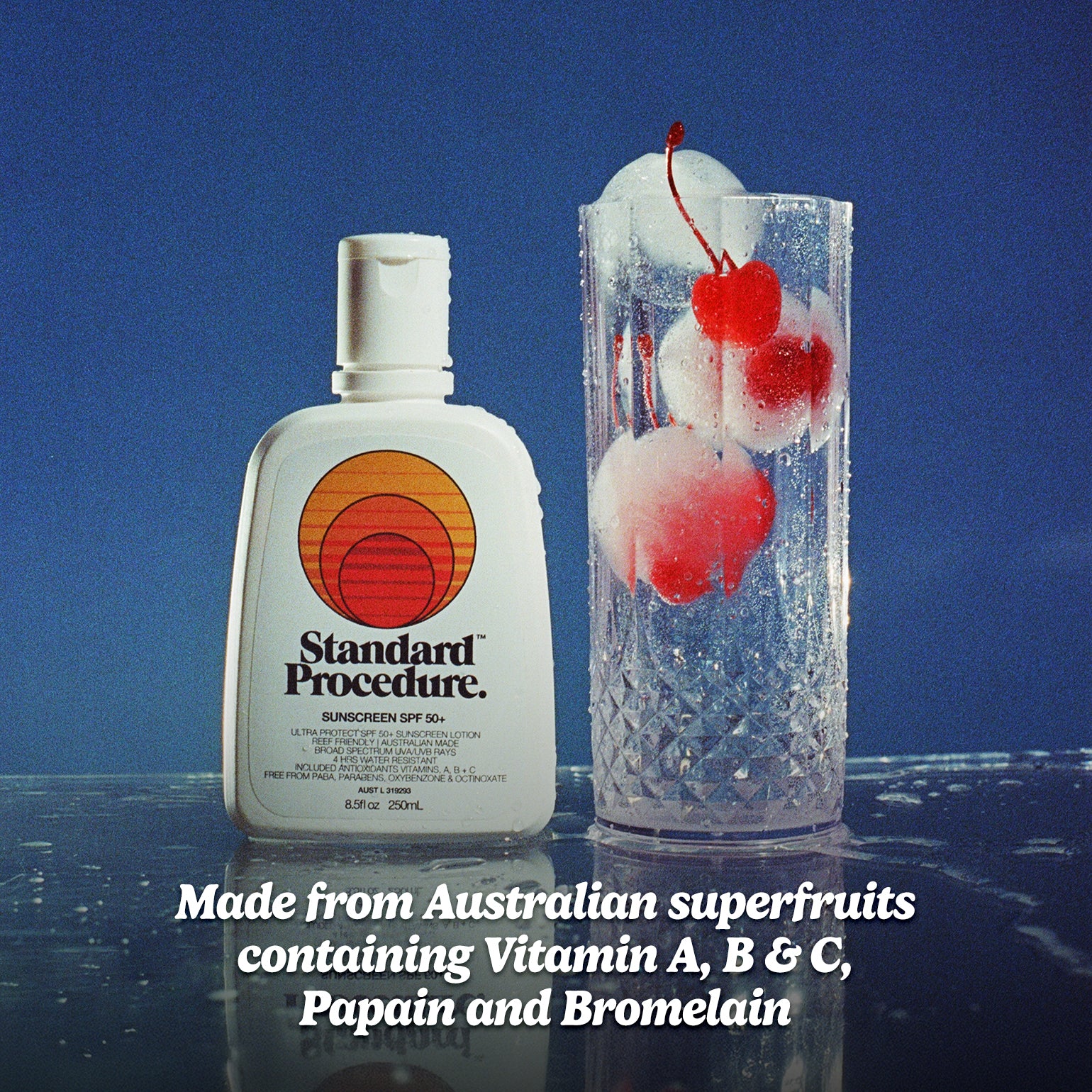 Organic SPF 50 sunscreen bottle beside a chilled glass of cherry sorbet on a reflective surface.