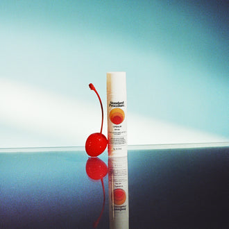 Lip protection SPF 50 balm displayed beside a red cherry on a reflective surface with a blue gradient background.