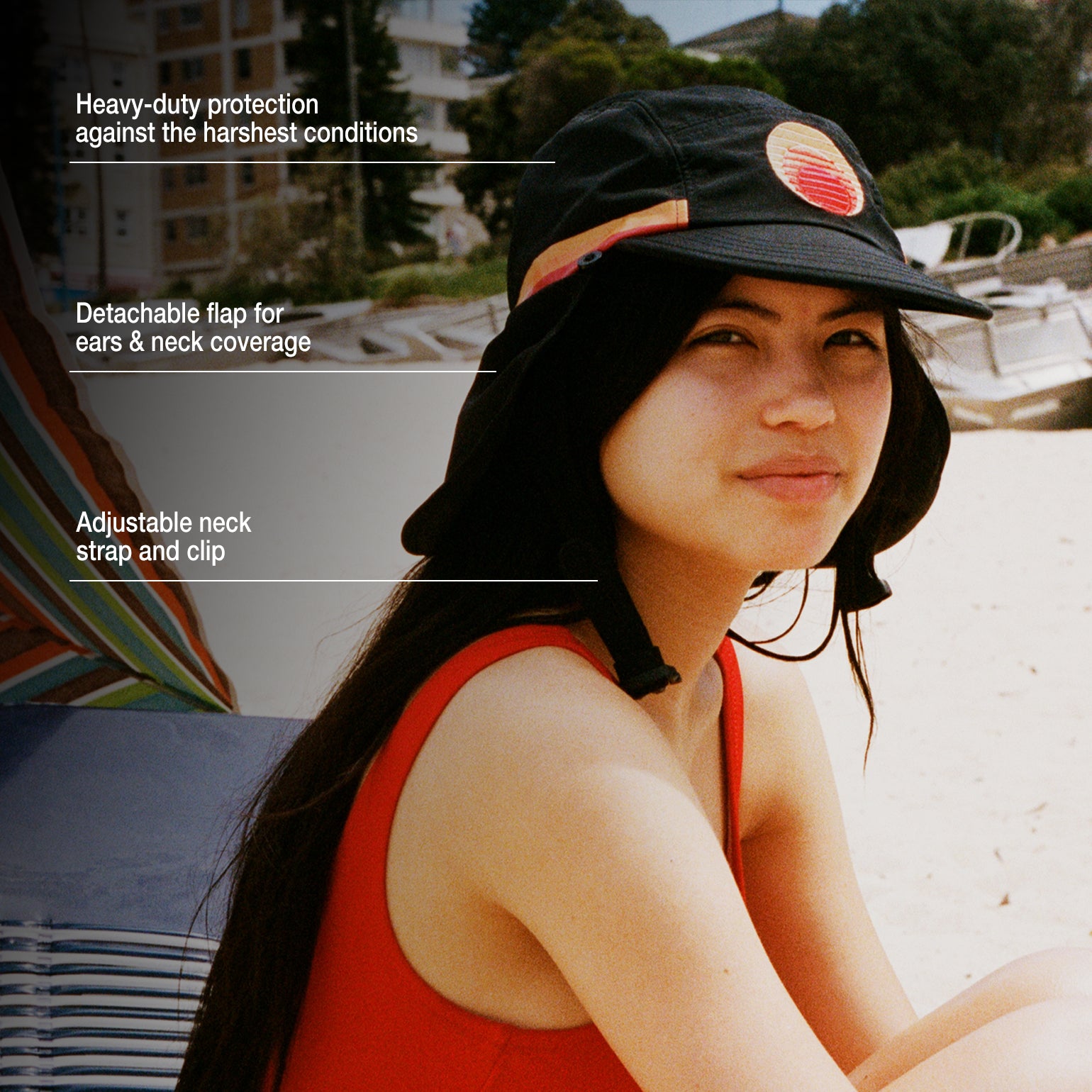 Black UPF 50+ sports hat with detachable neck flap and adjustable strap, worn at the beach.