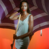 Editorial sun protection campaign for Standard Procedure SPF 15 moisturiser, model shaded under a striped parasol.