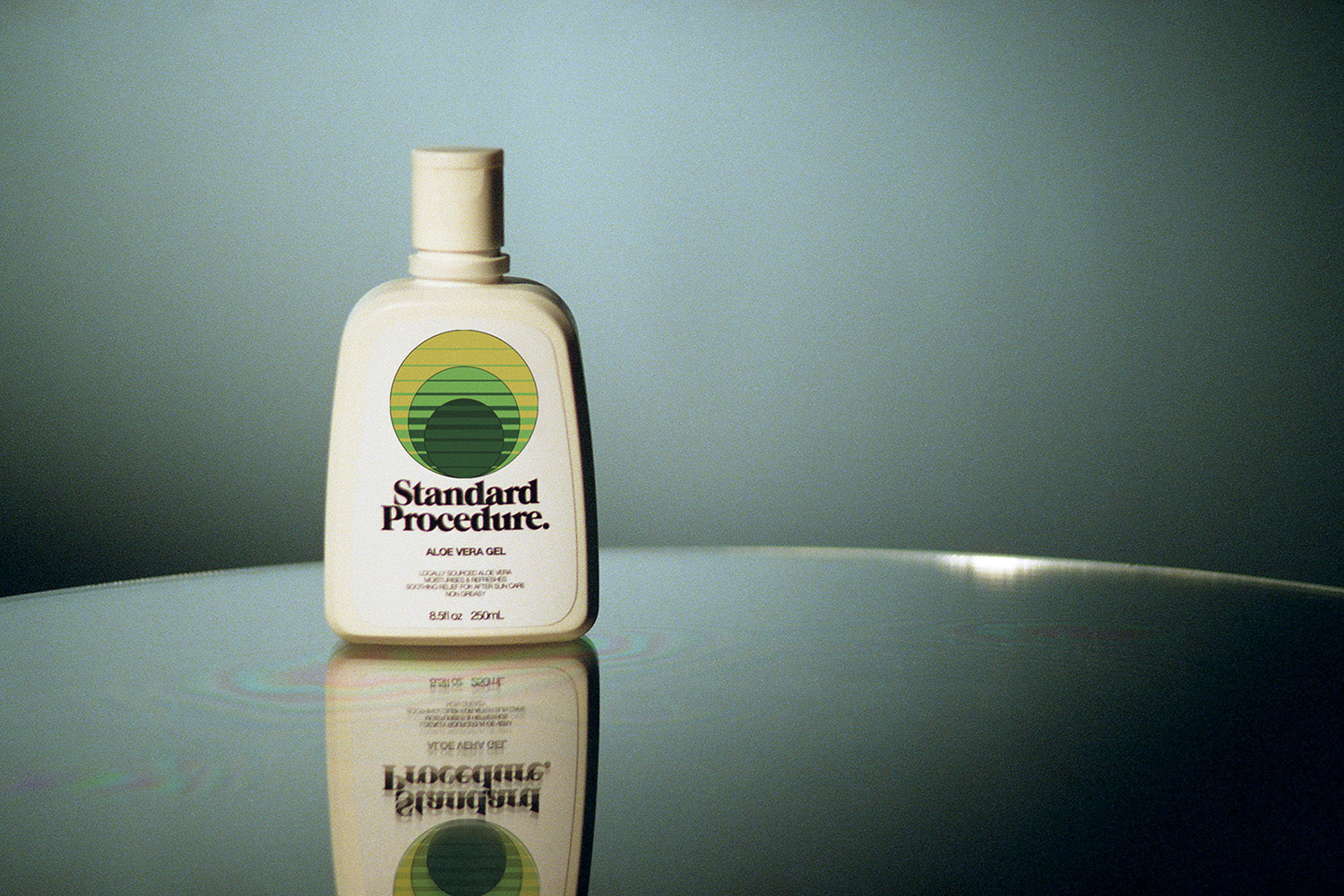Standard Procedure aloe vera gel 250ml bottle reflected on a glossy surface against a sage backdrop.