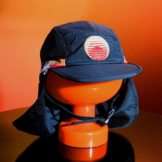 Navy UPF 50+ sports hat with neck flap and sunset patch on orange display stand.