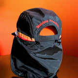 Rear view of black Standard Procedure flap cap with neck cover against an orange backdrop.