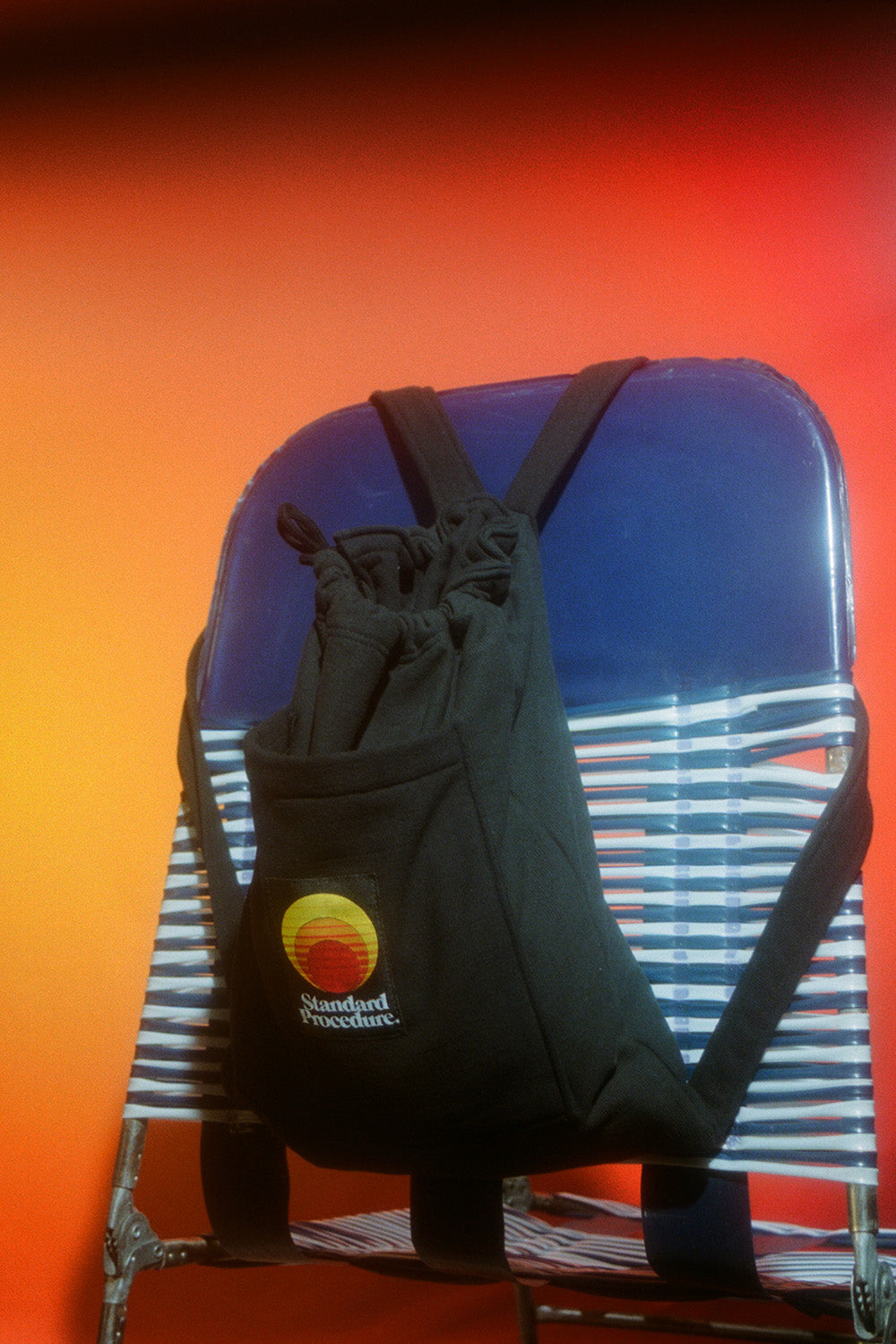Black Standard Procedure towel bag in backpack mode resting on a striped beach chair.