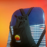 Black Standard Procedure towel bag in backpack mode resting on a striped beach chair.