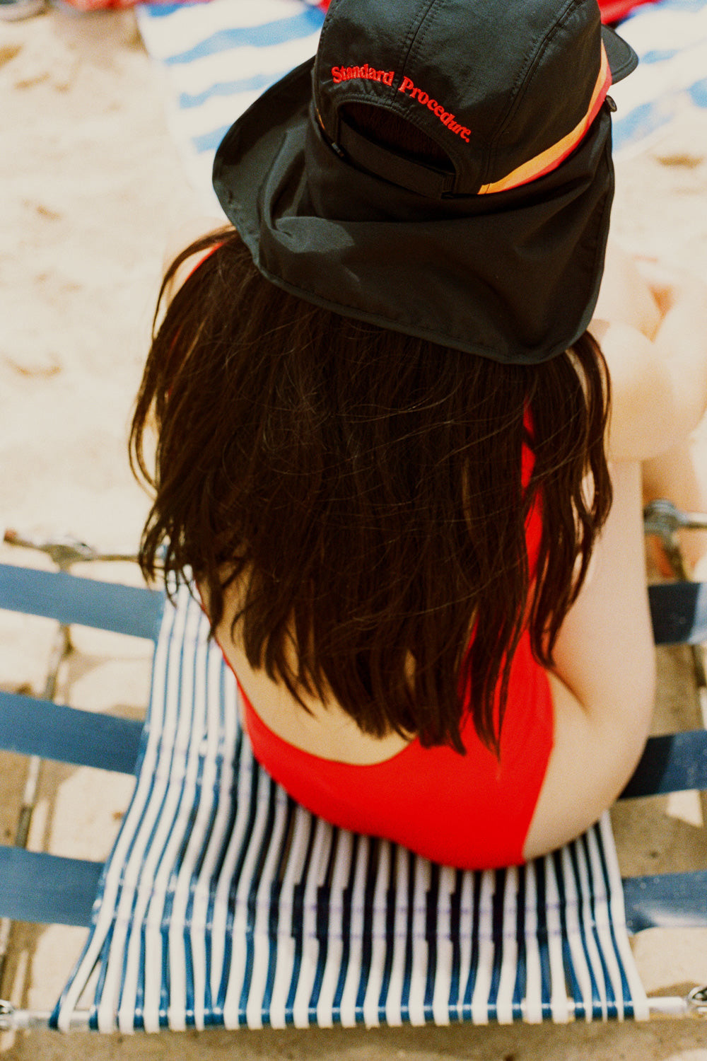 Black UPF 50+ sports hat with neck flap worn at the beach over a red swimsuit.
