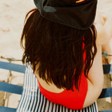 Black UPF 50+ sports hat with neck flap worn at the beach over a red swimsuit.