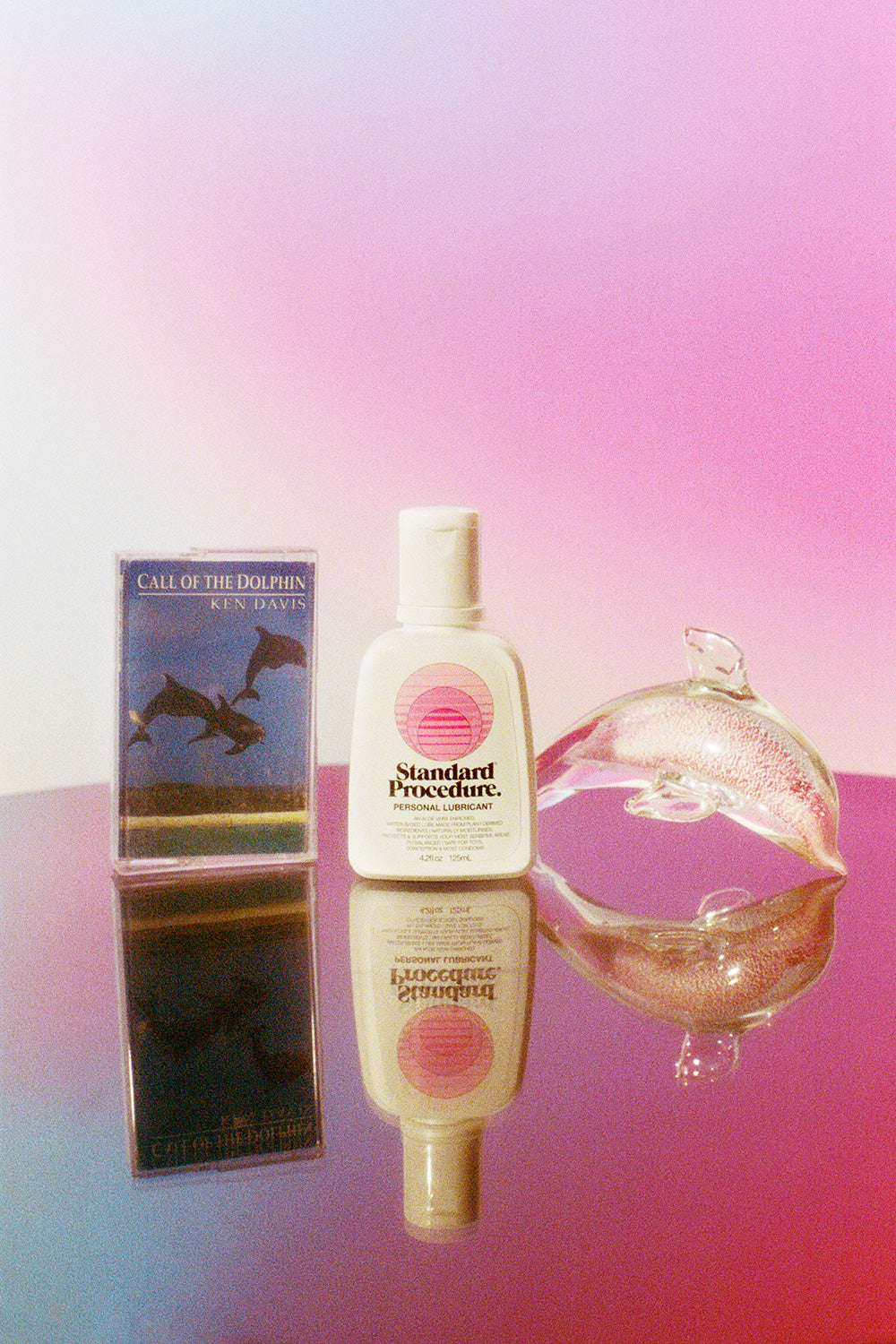 Standard Procedure Pleasure Jelly lubricant bottle beside a glass dolphin and Ken Davis cassette tape.