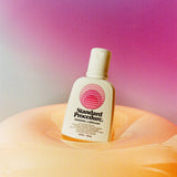 Aloe vera personal lubricant bottle nestled in a glossy peach inflatable against a pink purple gradient.
