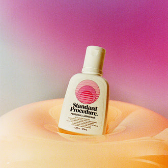 Aloe vera personal lubricant bottle nestled in a glossy peach inflatable against a pink purple gradient.