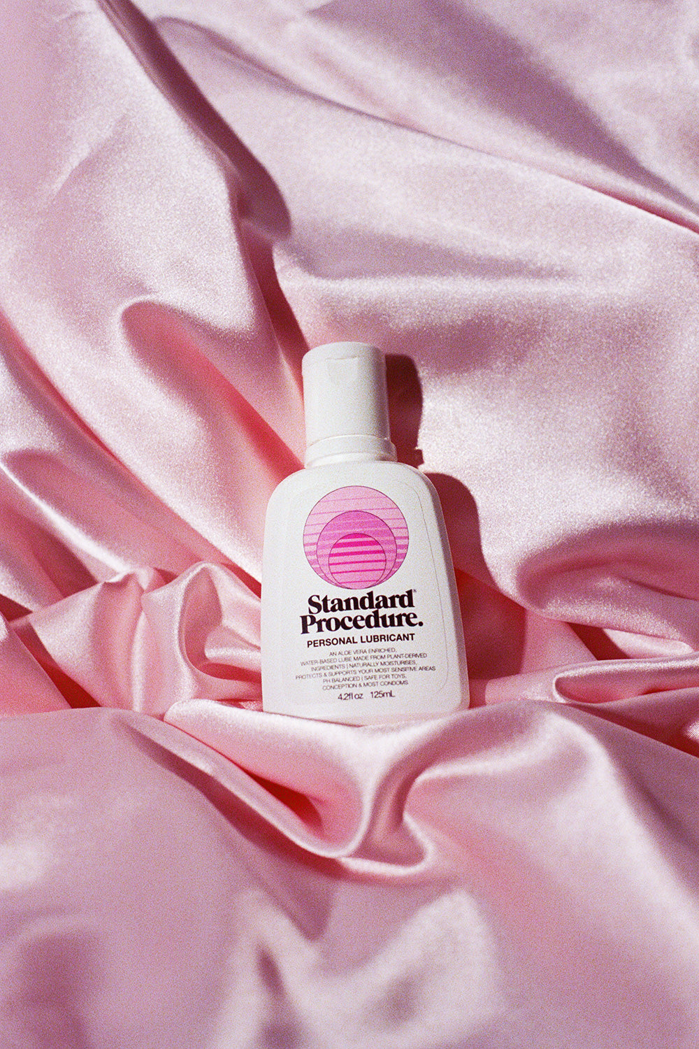 Standard Procedure aloe vera personal lubricant bottle nestled in draped pink satin sheets.