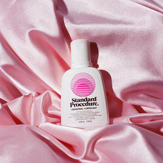Standard Procedure aloe vera personal lubricant bottle nestled in draped pink satin sheets.