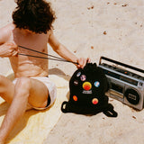 Person on a yellow beach towel cinching the Standard Procedure towel bag beside a vintage boombox.