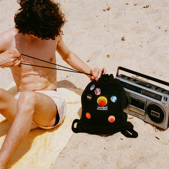Person on a yellow beach towel cinching the Standard Procedure towel bag beside a vintage boombox.