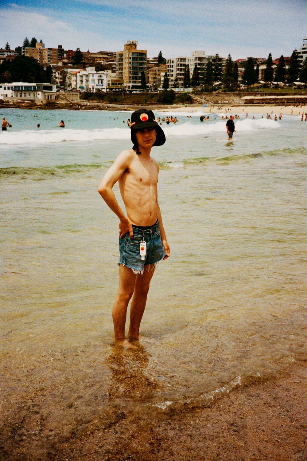 Black UPF 50+ sports hat with neck flap worn at a sunny beach shoreline.